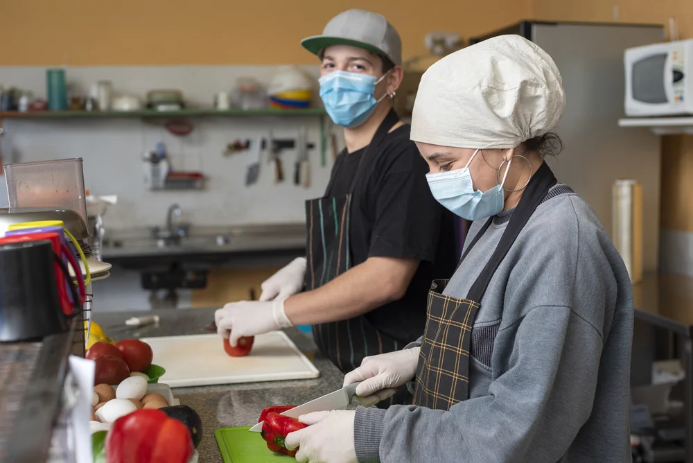 two-young-chefs-slicing-vegetables-wearing-medical-masks-1